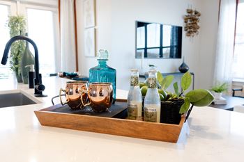 A wooden tray with a bottle of water, two glasses and a plant on a kitchen counter.